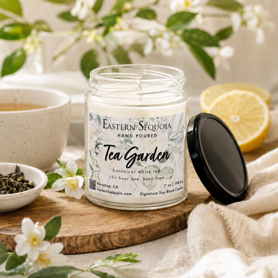 Candle labeled 'Tea Garden' by Eastern Sequoia on a wooden board with tea leaves, lemon, and flowers.
