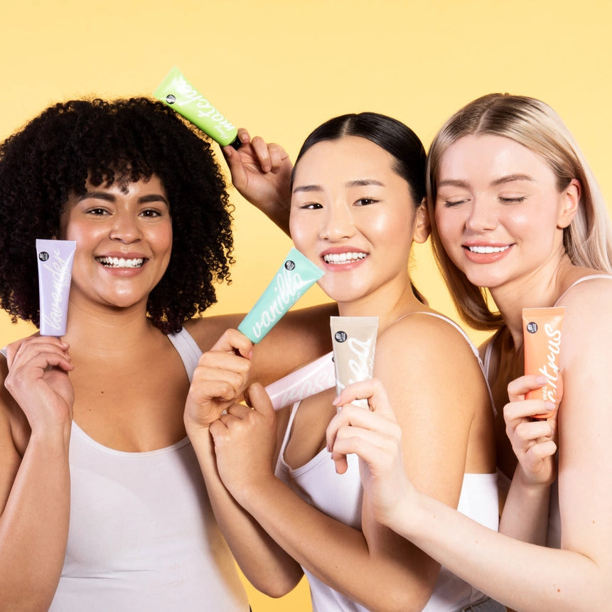 Three women holding skincare products against a yellow background