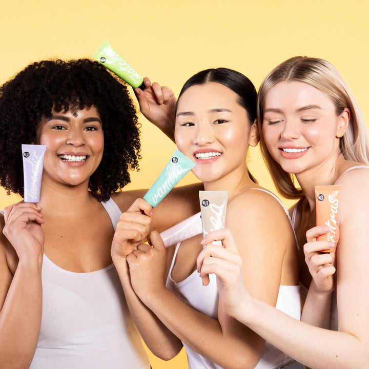 Three women holding skincare products against a yellow background