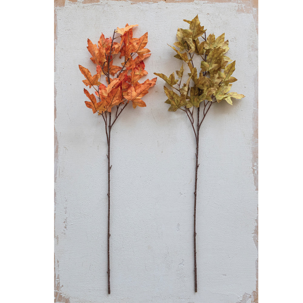 Two artificial leaf branches, one orange and one gold, on a textured white background.