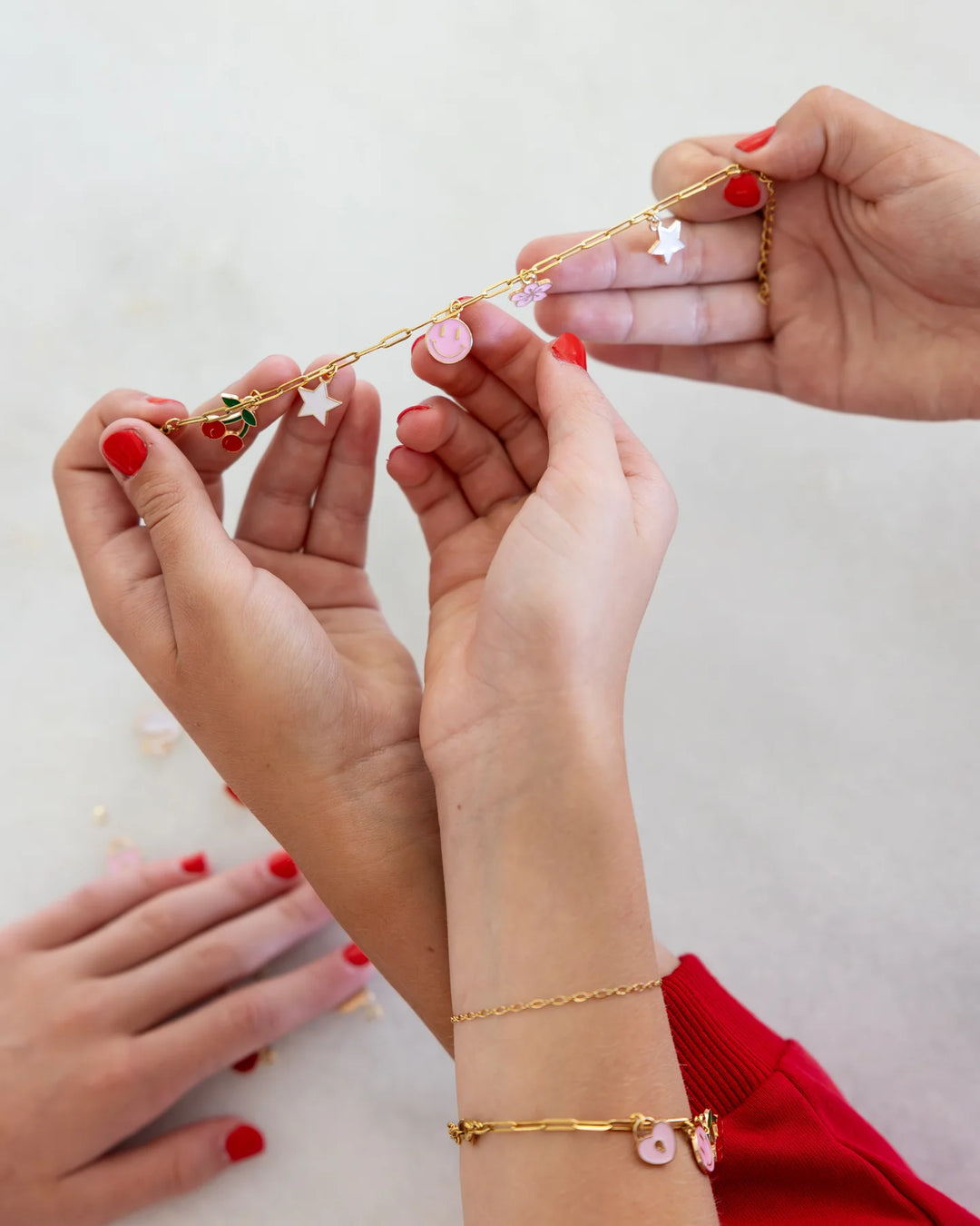 Close-up of hands wearing gold bracelets with pink accents on a light background