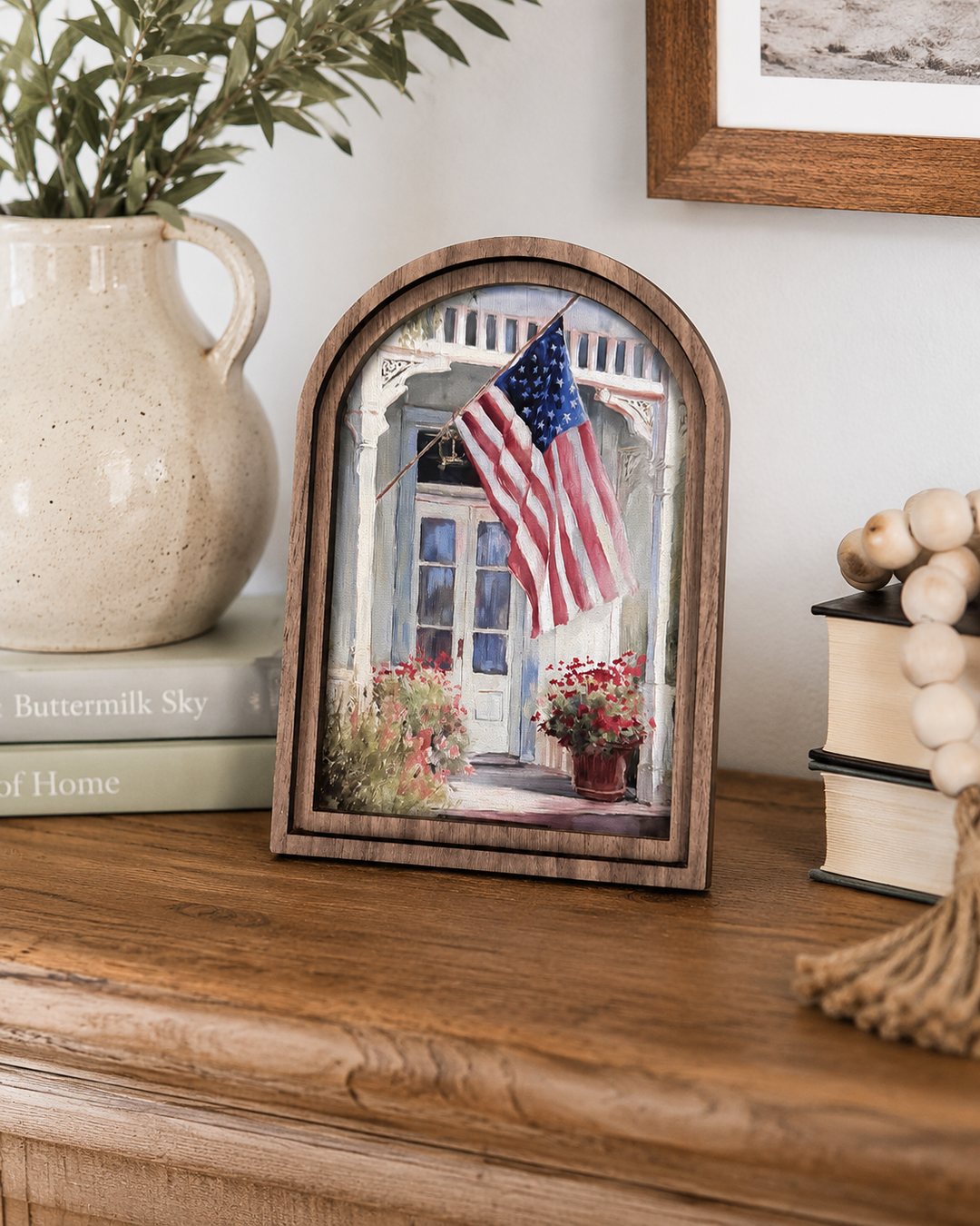Wooden frame with a picture of a house with an American flag on a wooden surface.