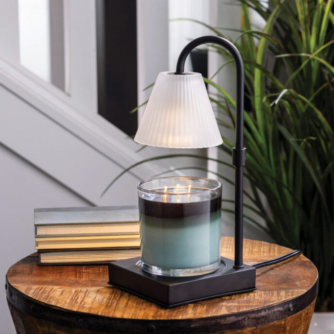 Candle with a lamp on a wooden table next to books and a plant