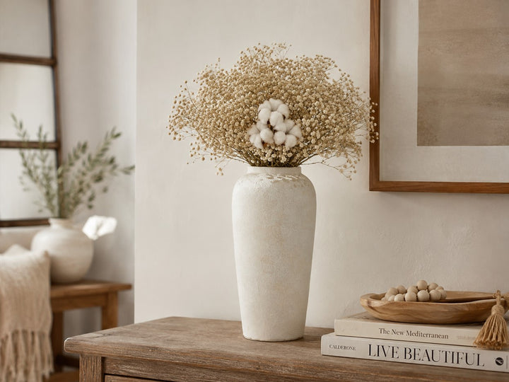 A tall textured off-white ceramic vase filled with dried baby&