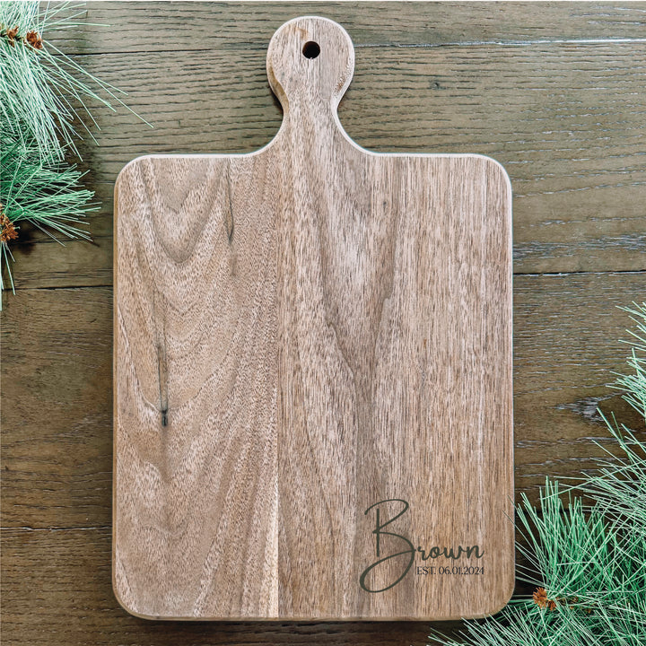 A personalized walnut cutting board with a handle, engraved with the name &