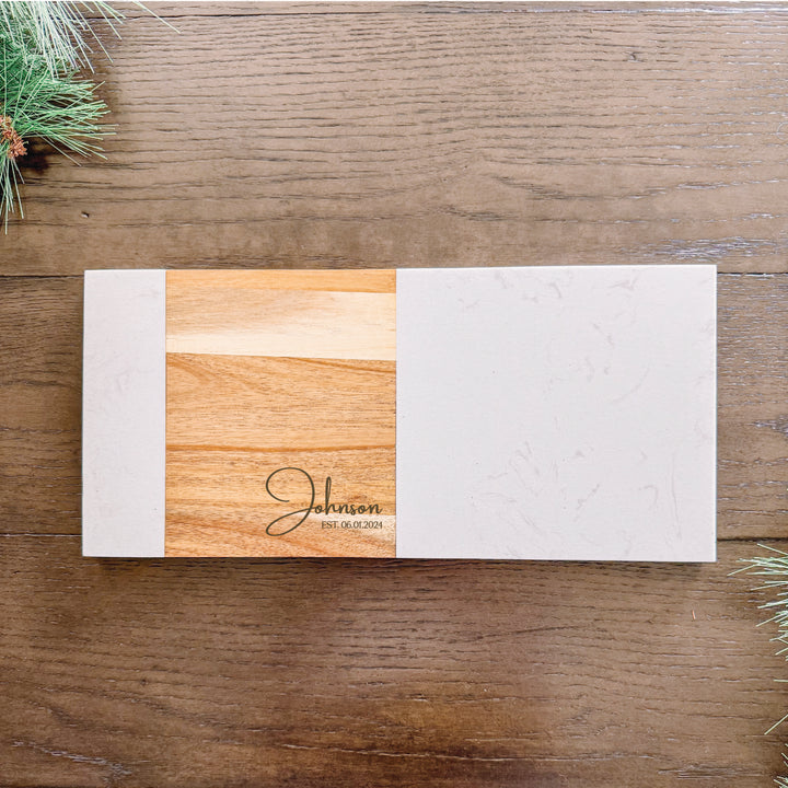 A personalized charcuterie board with a marble and acacia wood surface, featuring a engraved family name.
