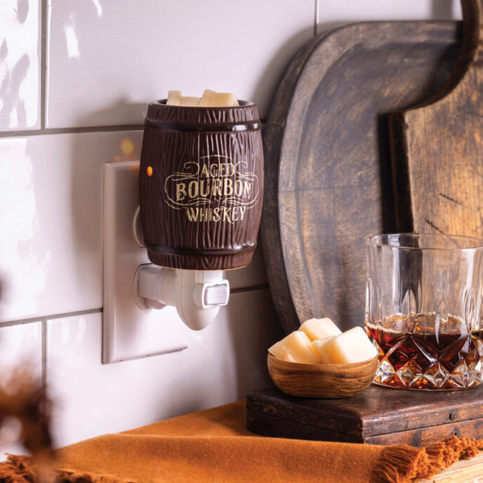 Bourbon whiskey warmer plugged into a wall socket with a glass of whiskey and a cutting board in the background.