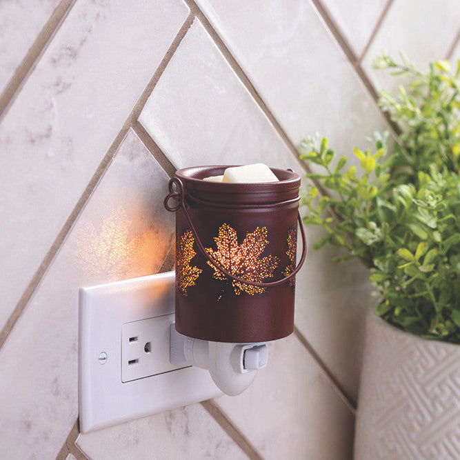 Wall-mounted candle warmer with decorative container on a tiled wall next to a plant.