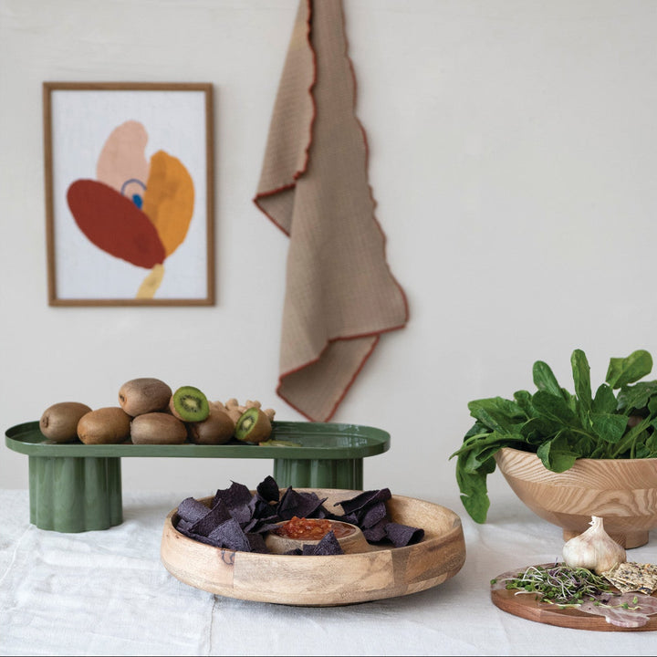 Decorative setting with a green stand, wooden bowl, and plants on a light surface.