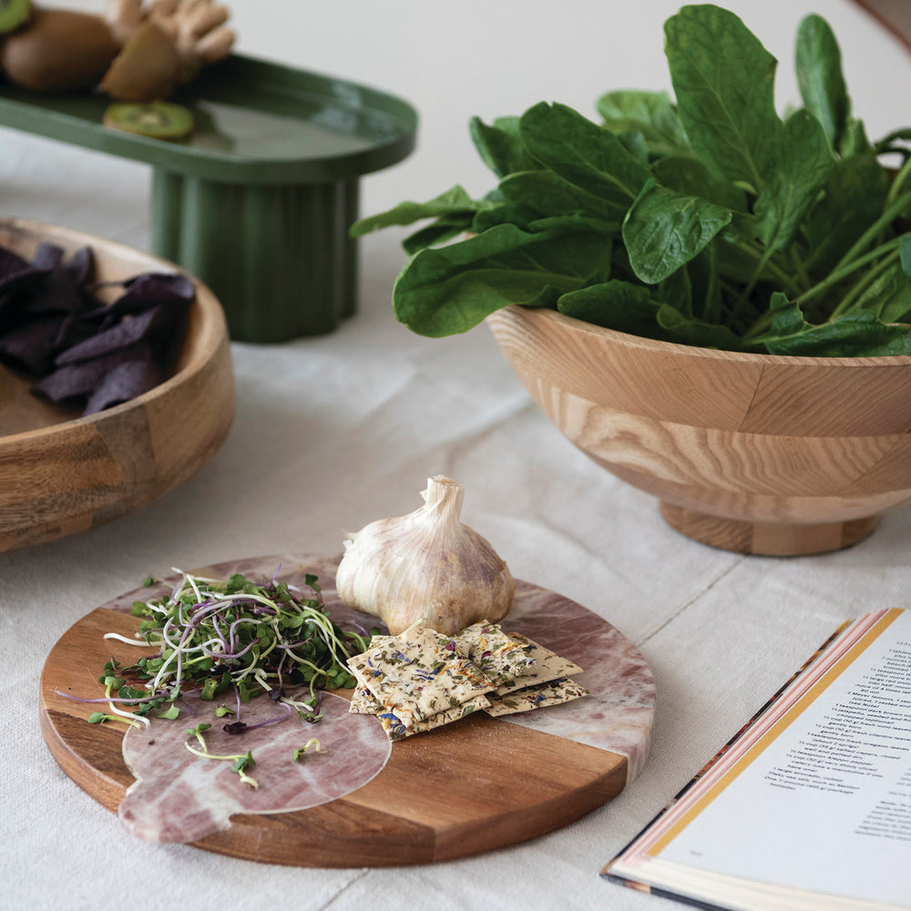 Wooden cutting board with cured meats, cheeses, and greens on a light wooden surface.