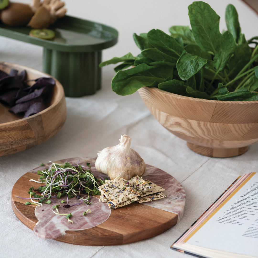 Wooden cutting board with cured meats, cheeses, and greens on a light wooden surface.