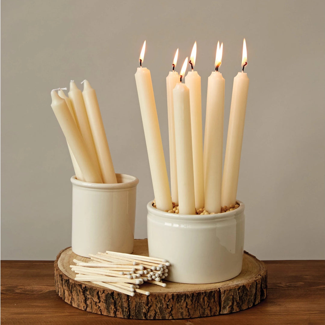 Two white candle holders with lit candles on a wooden surface.