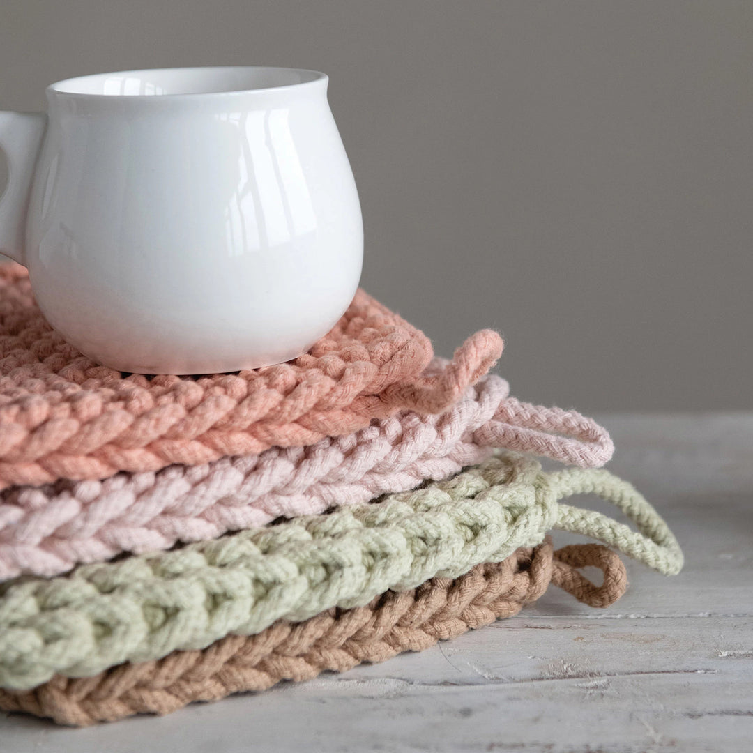 Stack of colorful knitted coasters with a white mug on a wooden surface.