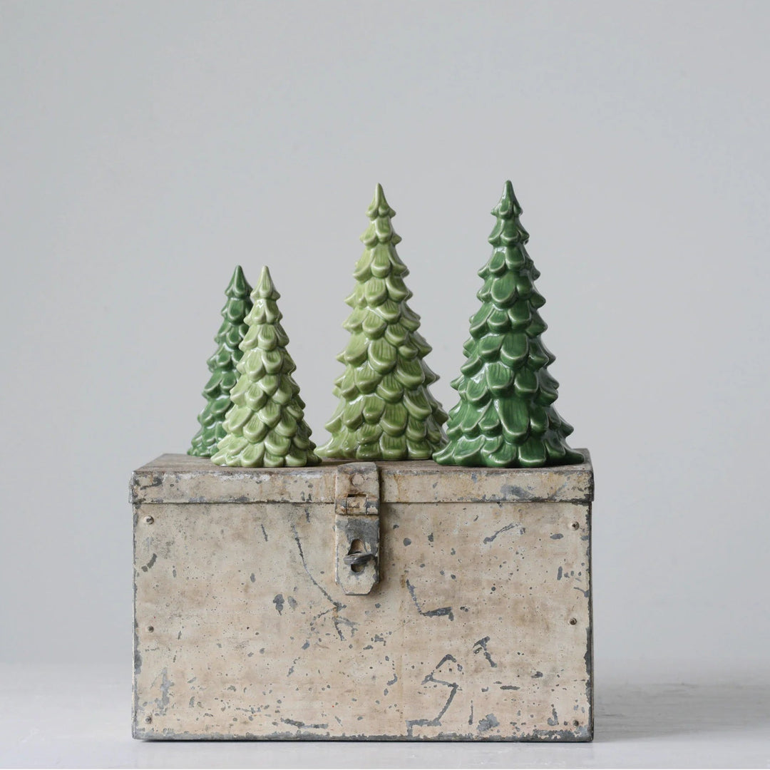 Three small textured green pine tree figurines arranged on top of a distressed beige stone-look rectangular box against a plain light gray studio background.